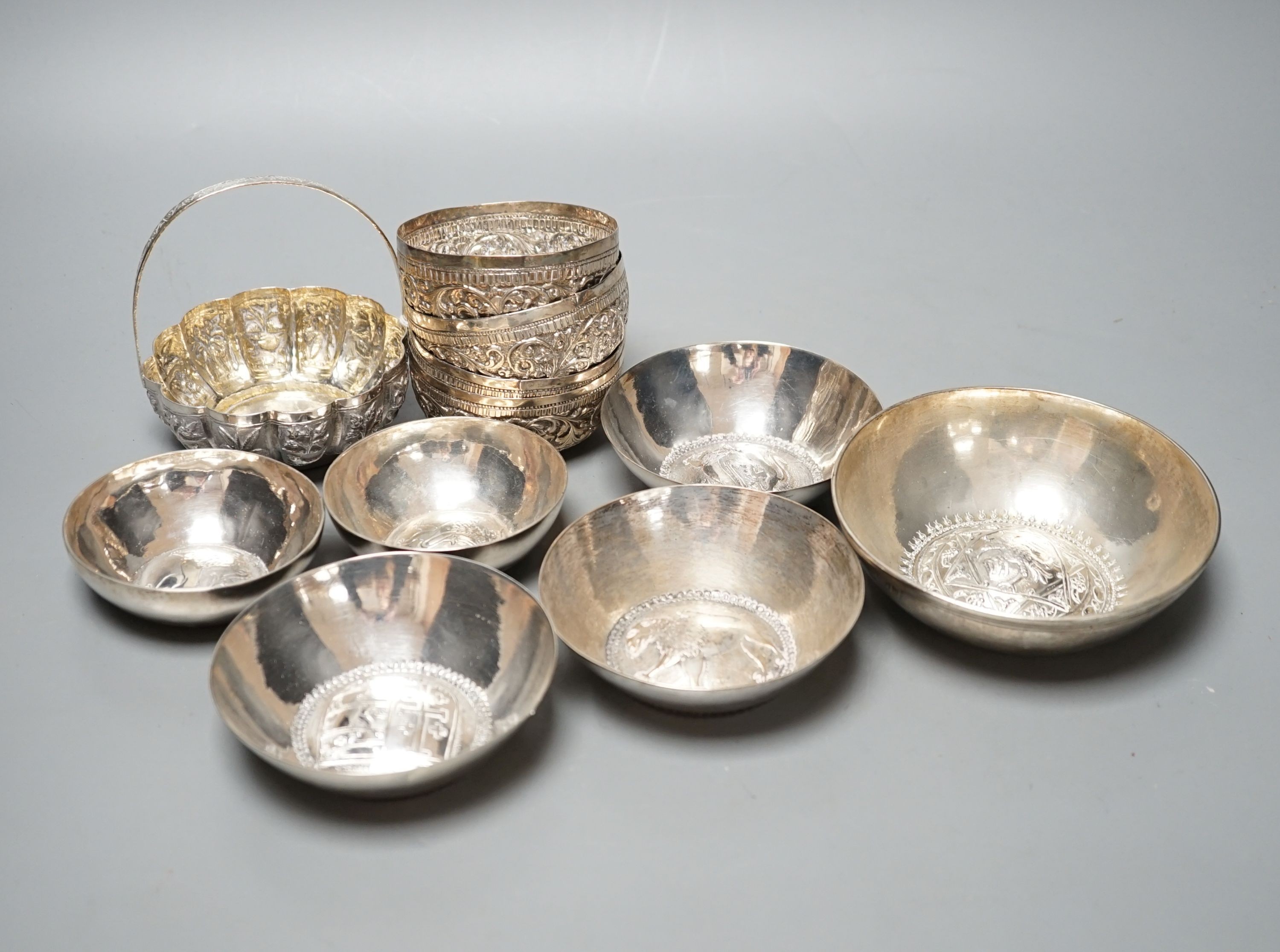 Four small Rangoon white metal bowls together with a simile basket and six small white metal bowls with heraldic motifs, gross 24.5oz.